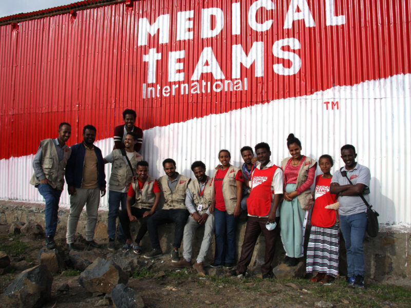 Group photo of staff and CHWs in front of the Medical Teams wall at the new clinic, 2022