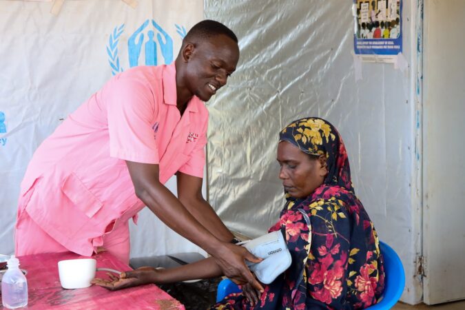 A nurse named Henry takes the blood pressure of a woman in triage at the welcome center in Uganda, 2024