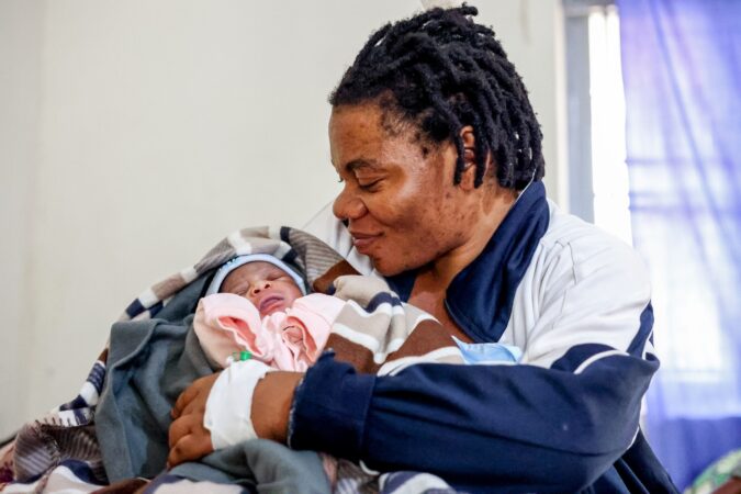 Rehema smiles looking at her newborn baby in the maternal health ward, Uganda, 2023