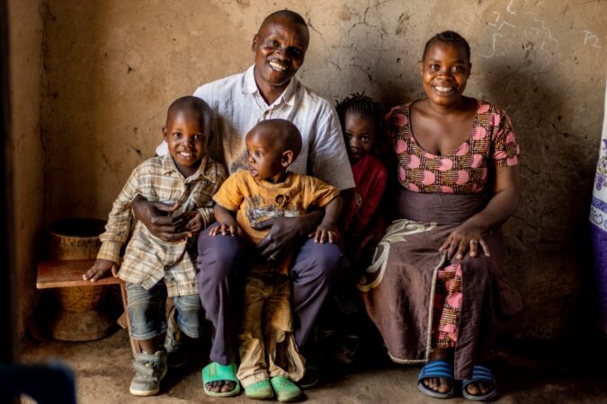 Obedi sits with his wife and children in his home in Uganda