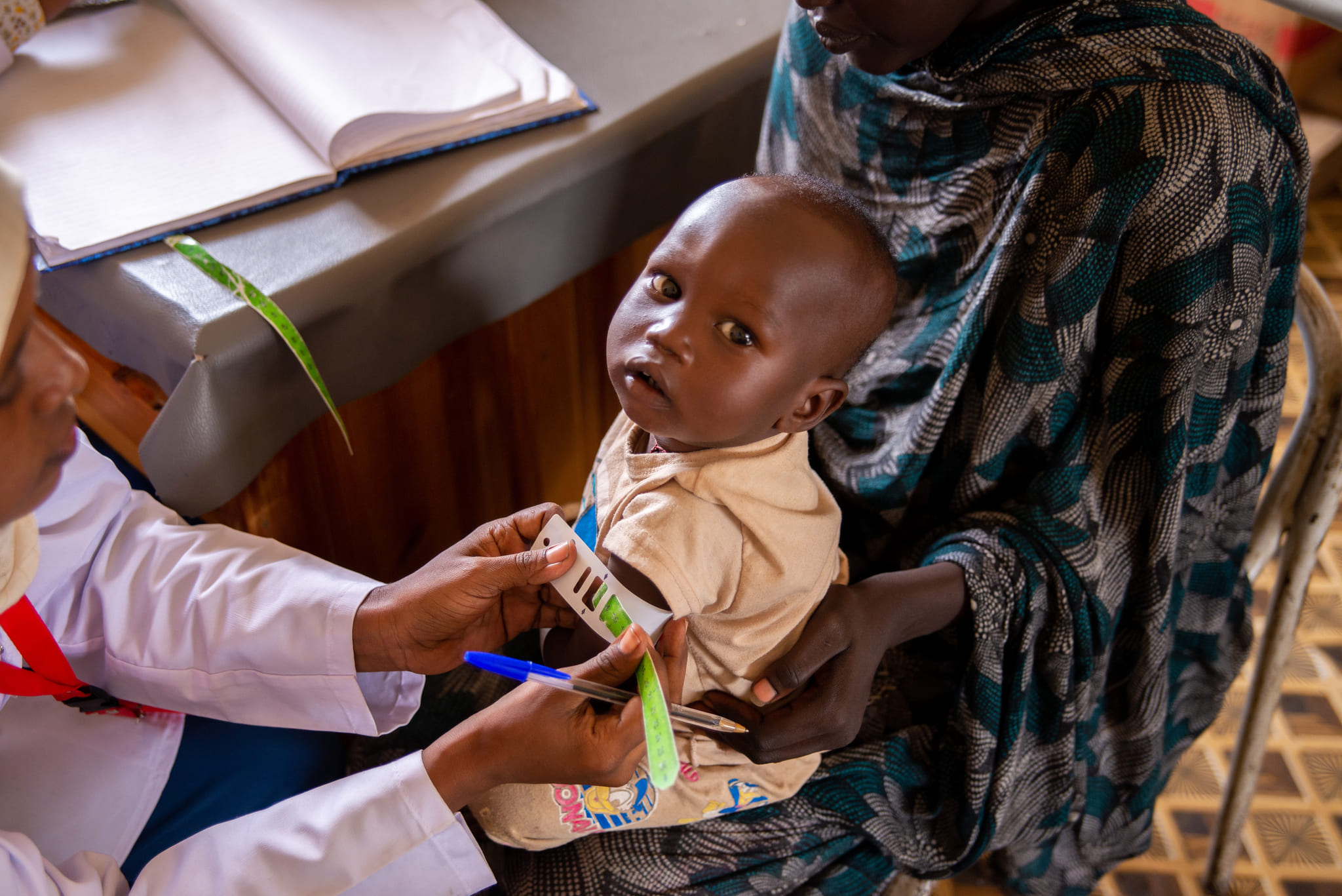 A nutrition assistant in Sudan measures a child's arm with MUAC tape