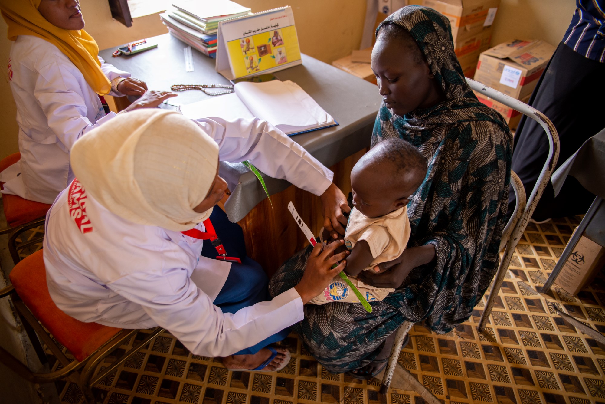 Ramadan receives a nutrition assessment while sitting on his mother's lap in a clinic