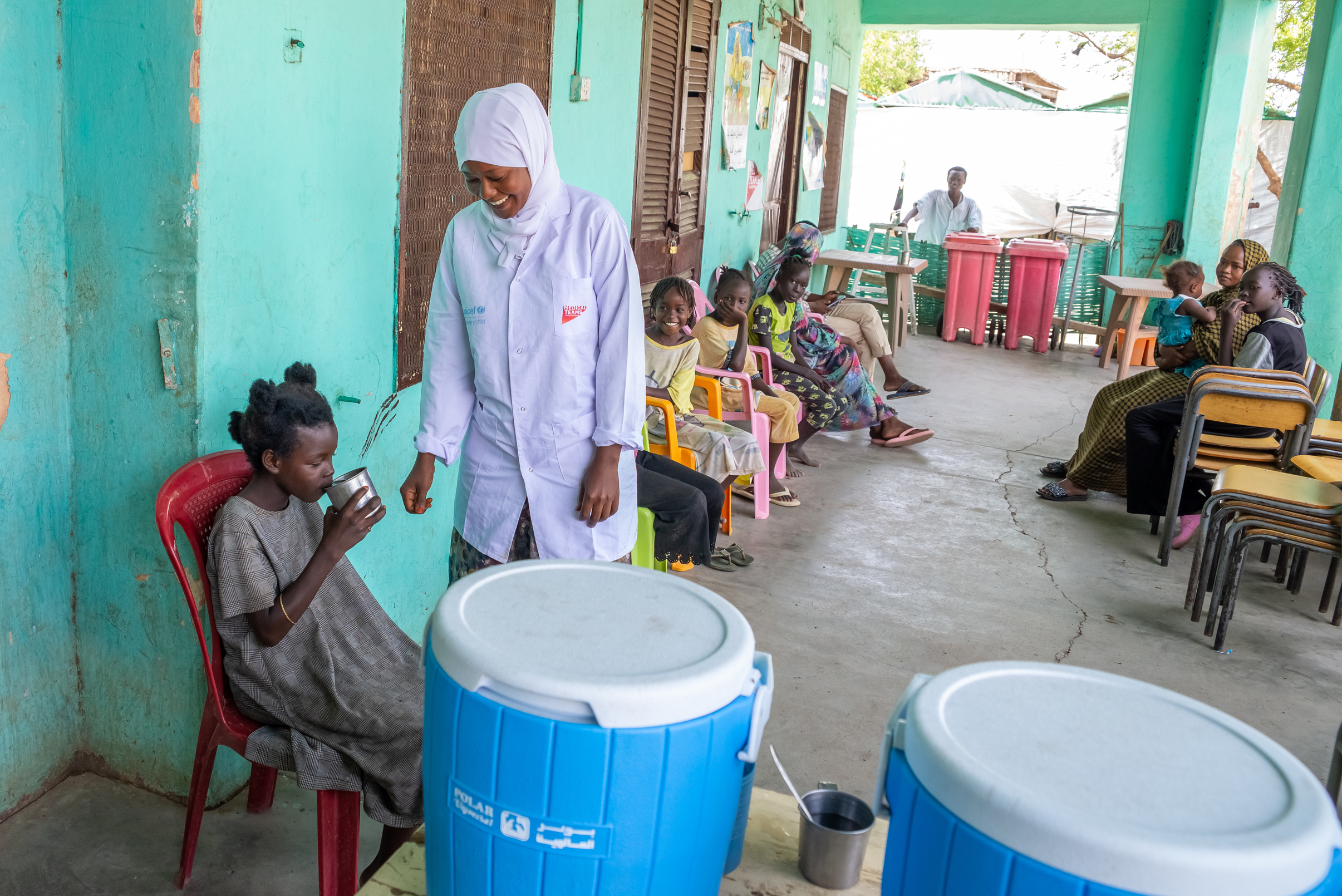 Mazahir smiles while providing young girl with ORS drink as other young girls wait.
