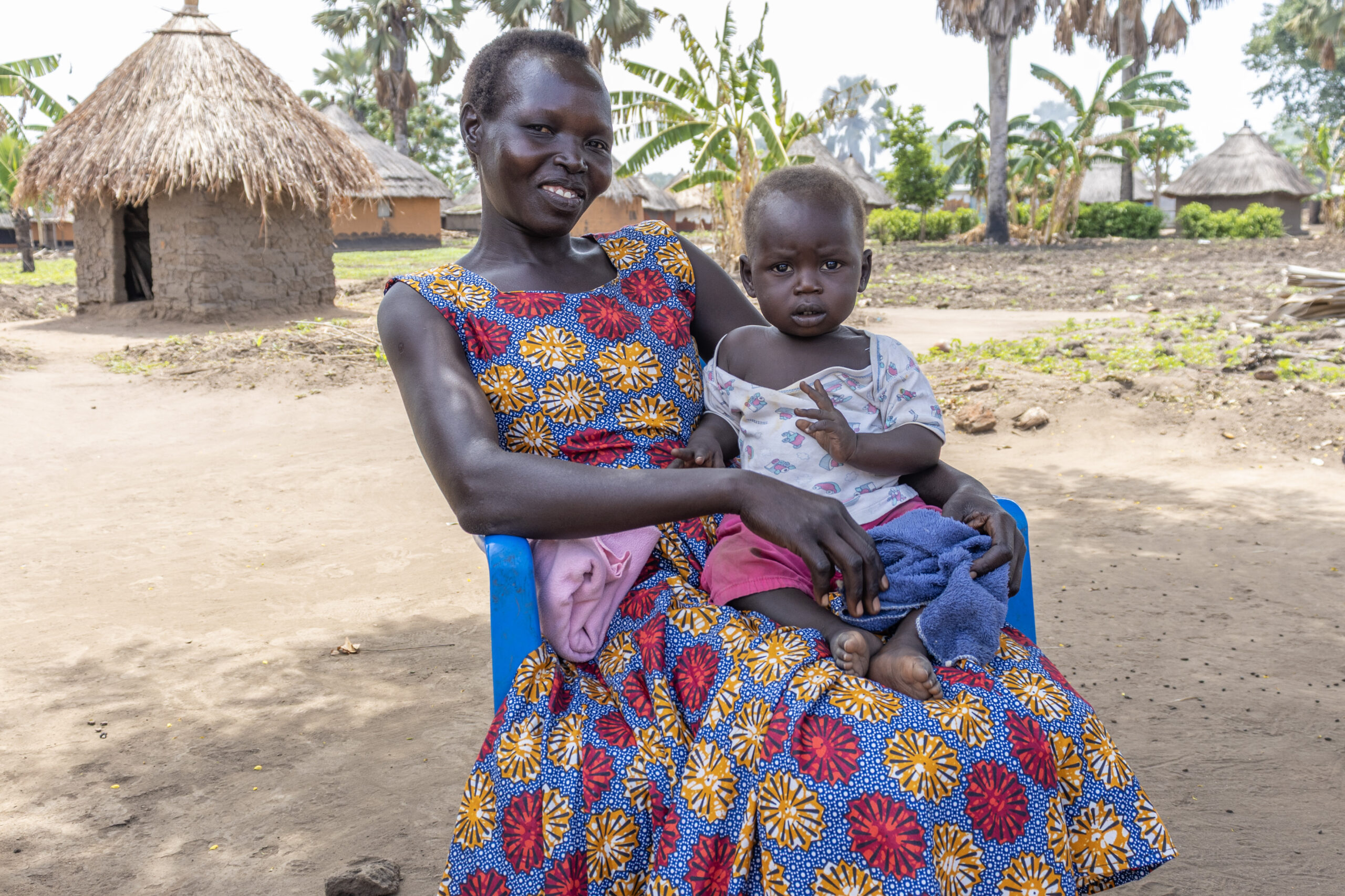 Beatrice Kideng holding her child in her lap outside of her home in Palorinya. 