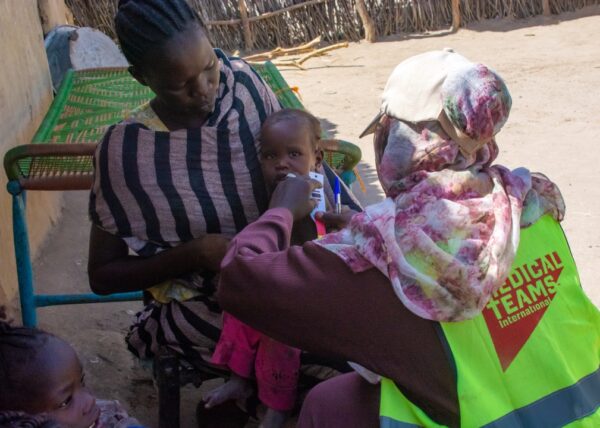 A Medical Teams health worker checks a child's nutrition using MUAC tape measuring arm circumference outside in Sudan.