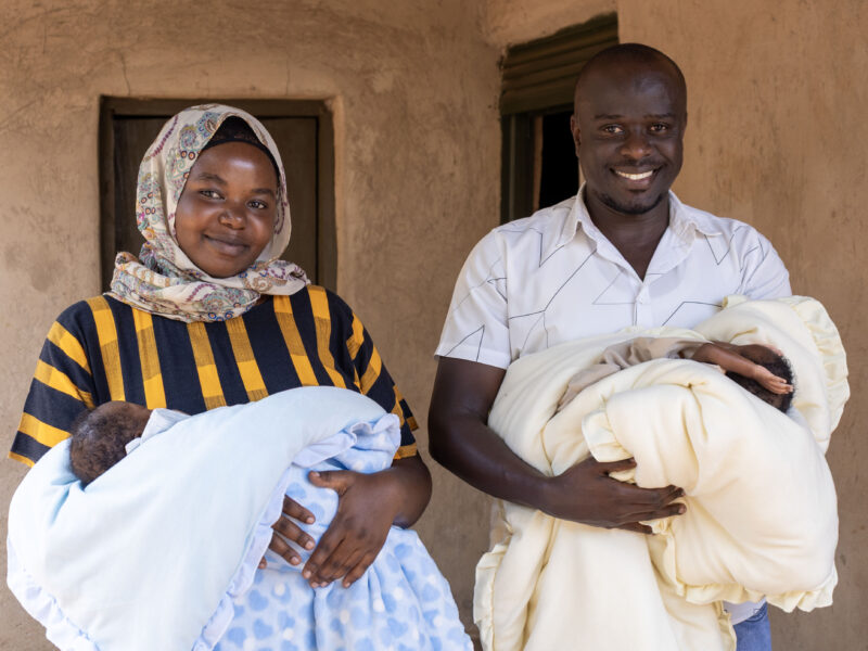 Jamil & Leila holding twins smiling at camera.