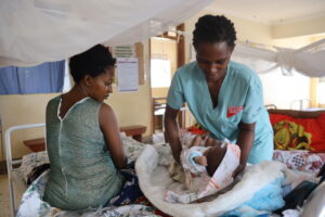 In Uganda, a midwife holds a new baby while the mother looks on. 